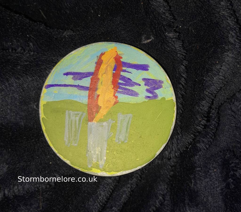A small painted stone representing a fire sticking the earth near standing stones 