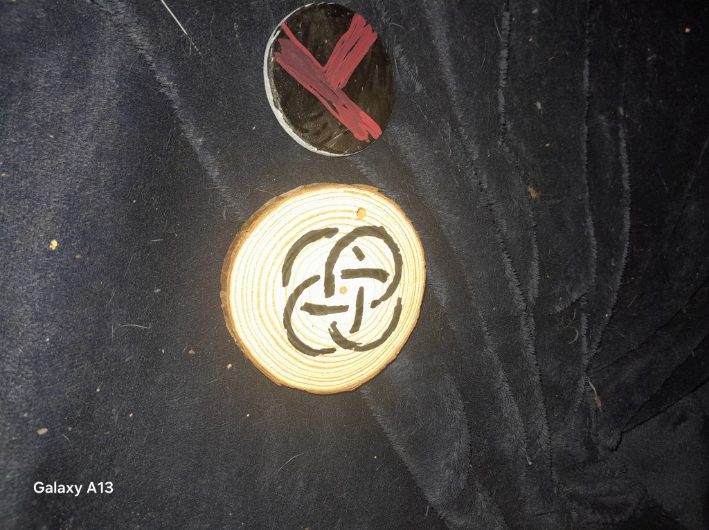 An image of a wooden rune stone featuring intricate black designs placed on a dark, textured fabric.