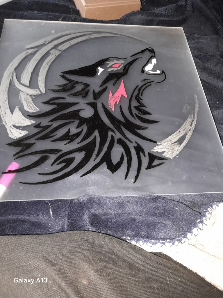 A hand-painted artwork featuring a stylized black wolf's head with red accents, set against a transparent background, resting on a dark fabric surface.