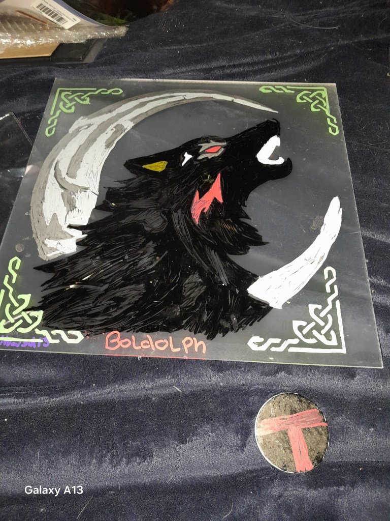 A hand-painted piece featuring a black wolf howling against a moon with Celtic designs, accompanied by a painted rune stone.