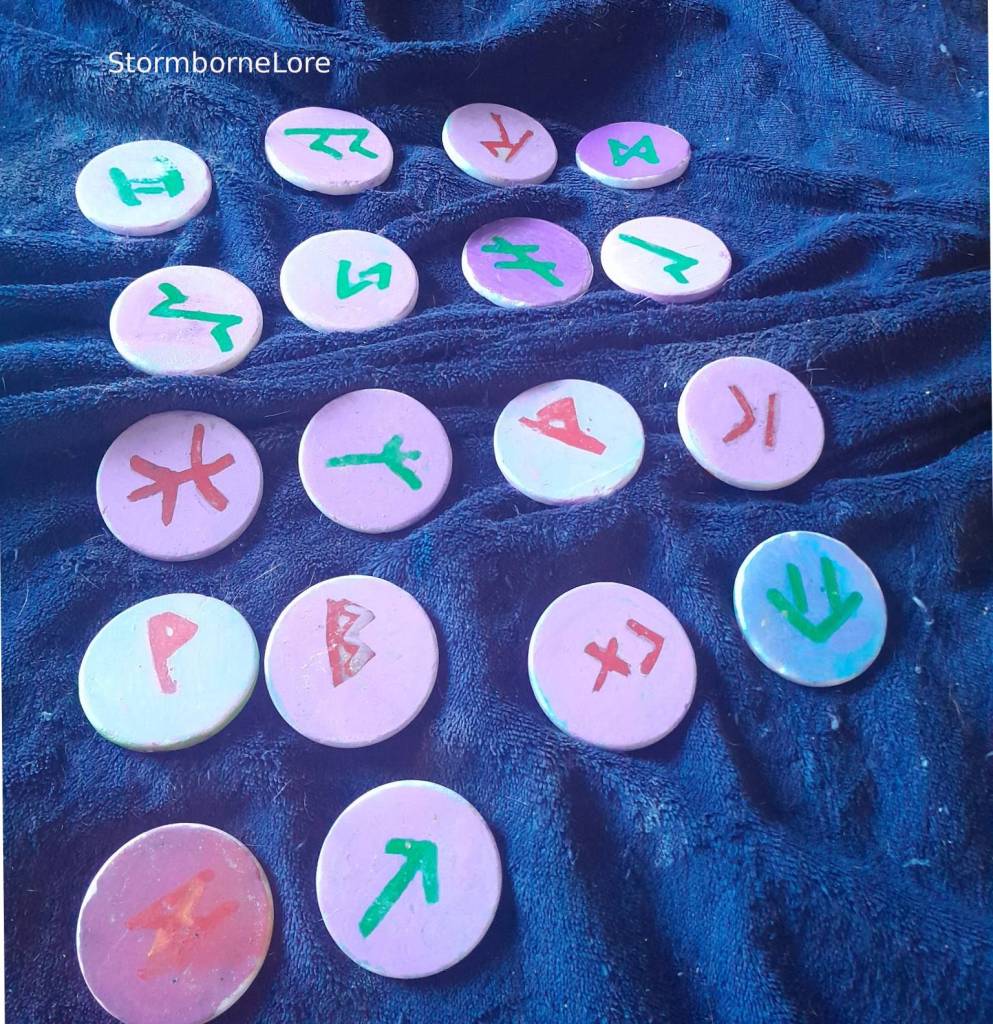 A collection of hand-painted rune stones displayed on a dark blue fabric, featuring various symbols and designs in different colors.