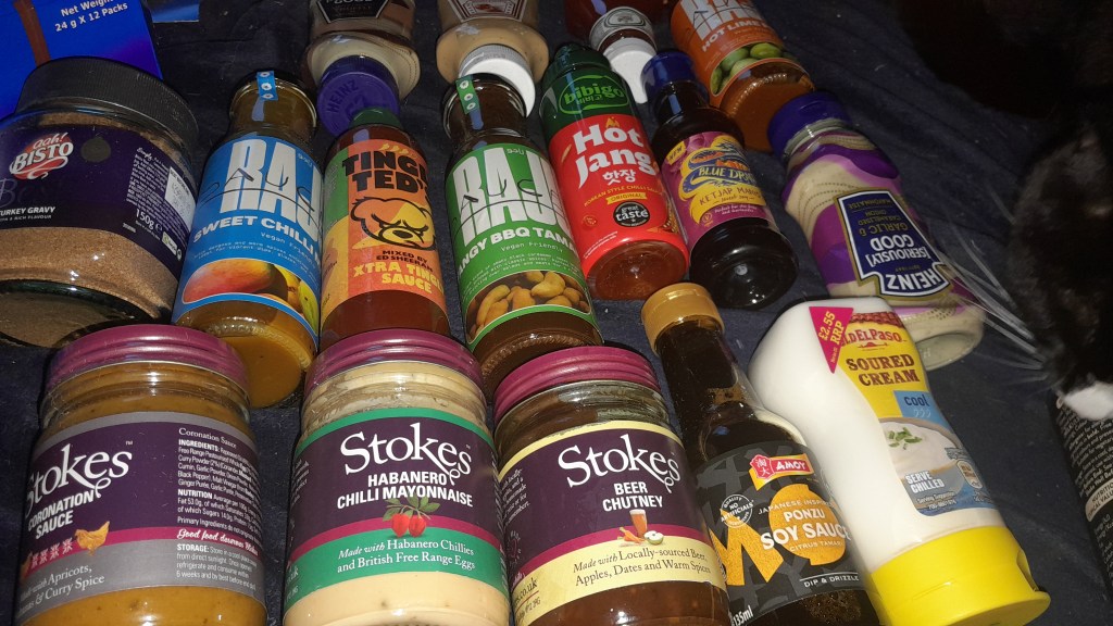 A variety of condiment bottles and jars arranged on a surface, including sauces, gravies, and mayonnaises in colorful packaging.