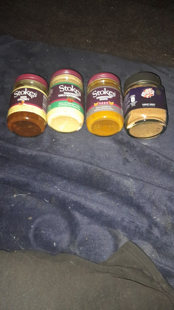 Four jars of sauces on a dark background, including Stokes Beer Chutney, Habanero Chilli Mayo, Coronation Sauce, and a jar of Bisto turkey gravy.